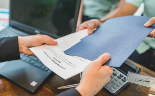 Agent immobilier remettant des documents imprimés à un client lors d’une négociation.