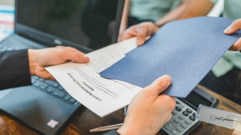 Agent immobilier remettant des documents imprimés à un client lors d’une négociation.